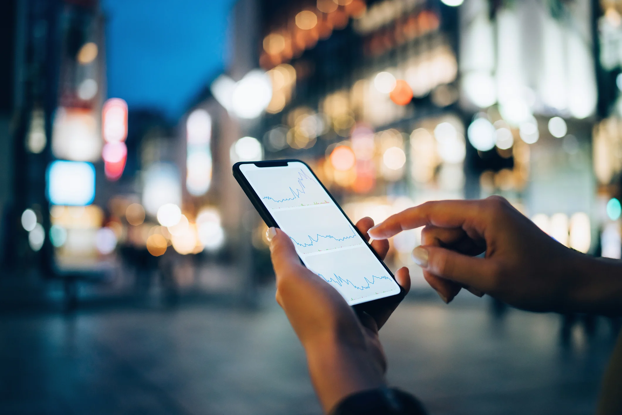 Persona revisando gráficos de activos digitales en el teléfono, de noche, en una ciudad